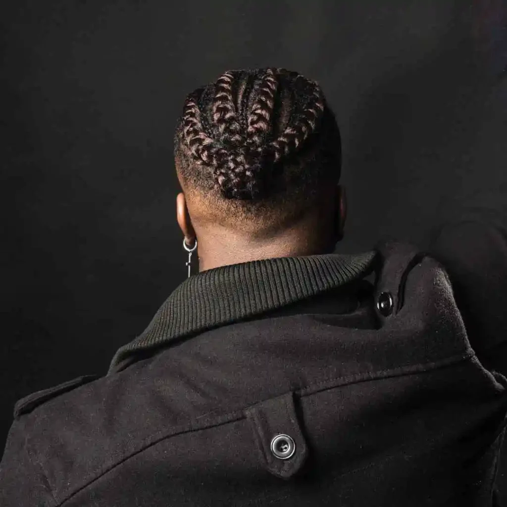 A close-up of a person from the back, showcasing intricate MEN HAIRSTYLE CORNROW braided hairstyles and wearing a black coat with a high collar.