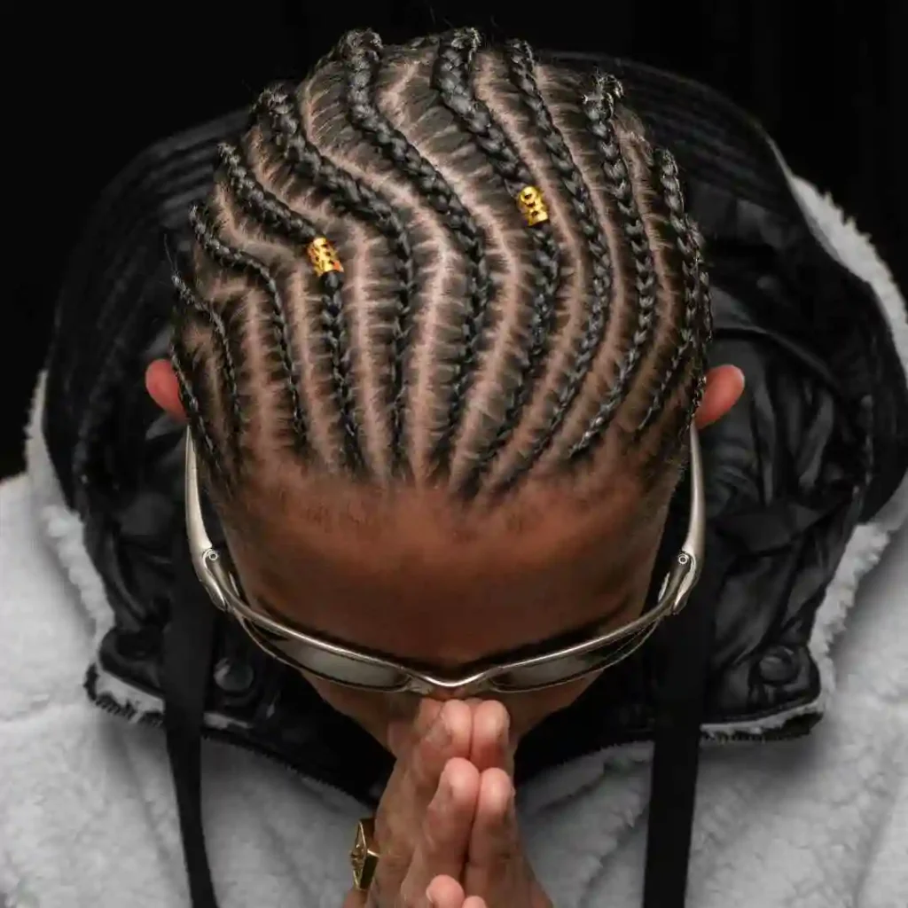 The Ultimate Guide to Men Hairstyles Cornrow- Sizzling Styles of Braided Looks 2 Person with intricate men hairstyle cornrow, adorned with gold beads, bows their head in prayer while wearing sunglasses.