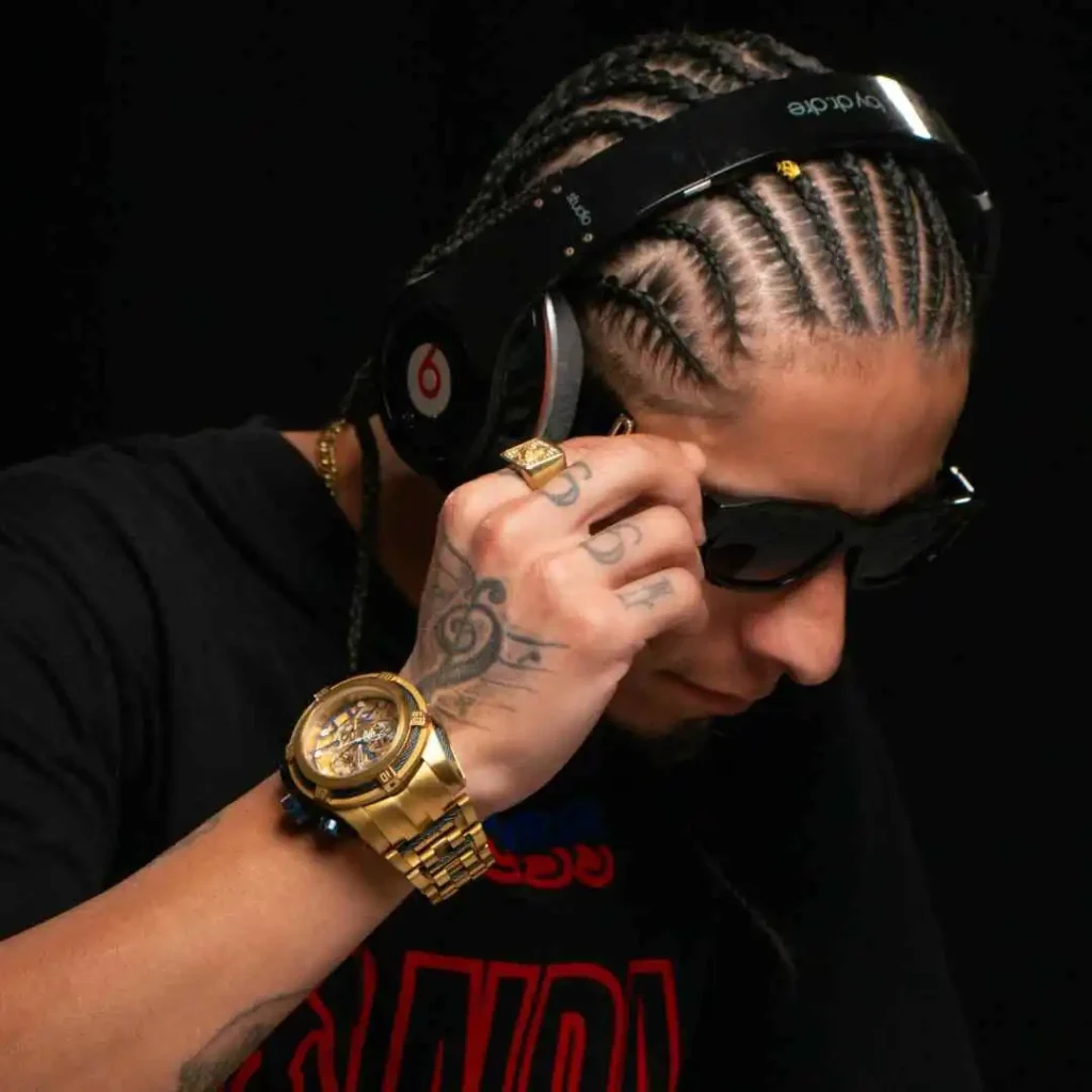 A person wearing black headphones and a stylish black shirt showcases multiple gold rings and a large gold watch on their wrist, highlighting a trendy men hairstyle cornrow.