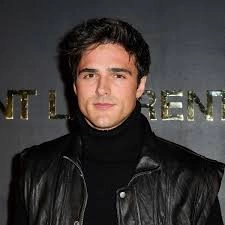 A person with Men Hairstyles Curls poses against a dark backdrop with the text 'SAINT LAURENT,' wearing a black leather jacket and a turtleneck.