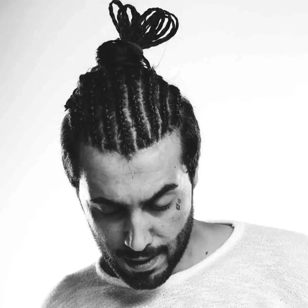 A person with braided hair styled into a bun, showcasing Men Hairstyles Curls, wearing a light sweater, against a bright white background.