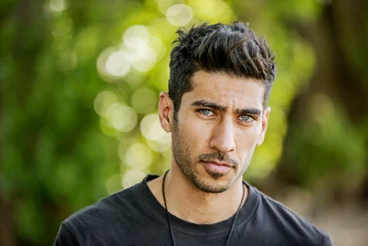 Men Hairstyles Indian- Trendy Looks For Your Unique Personality 8 A young man showcasing trendy men hairstyles Indian style, with stylish, tousled dark hair, stands outdoors surrounded by a backdrop of lush green foliage and soft, blurred light.