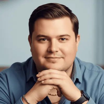 How to Choose the Best Haircut for Your Face Shape Men 6 A person sitting with hands clasped together, wearing a blue shirt and a watch, showcasing the best haircut for your face shape men, against a softly blurred background.