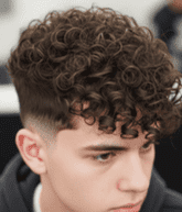 A young man with curly hair sits in a salon chair